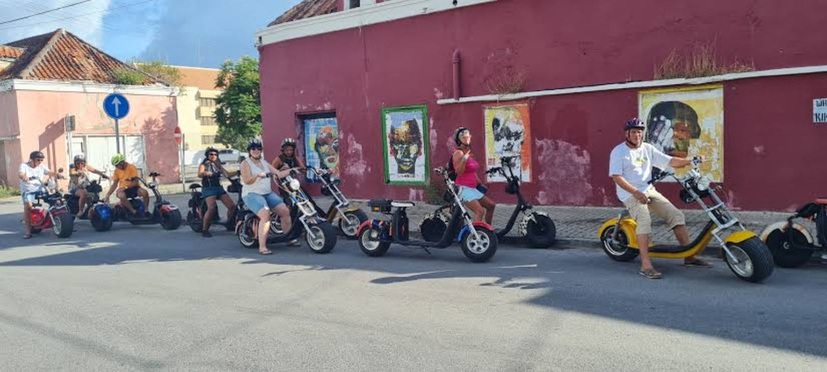Group riding colorful Iguana Ride electric scooters through Otrobanda, Curaçao